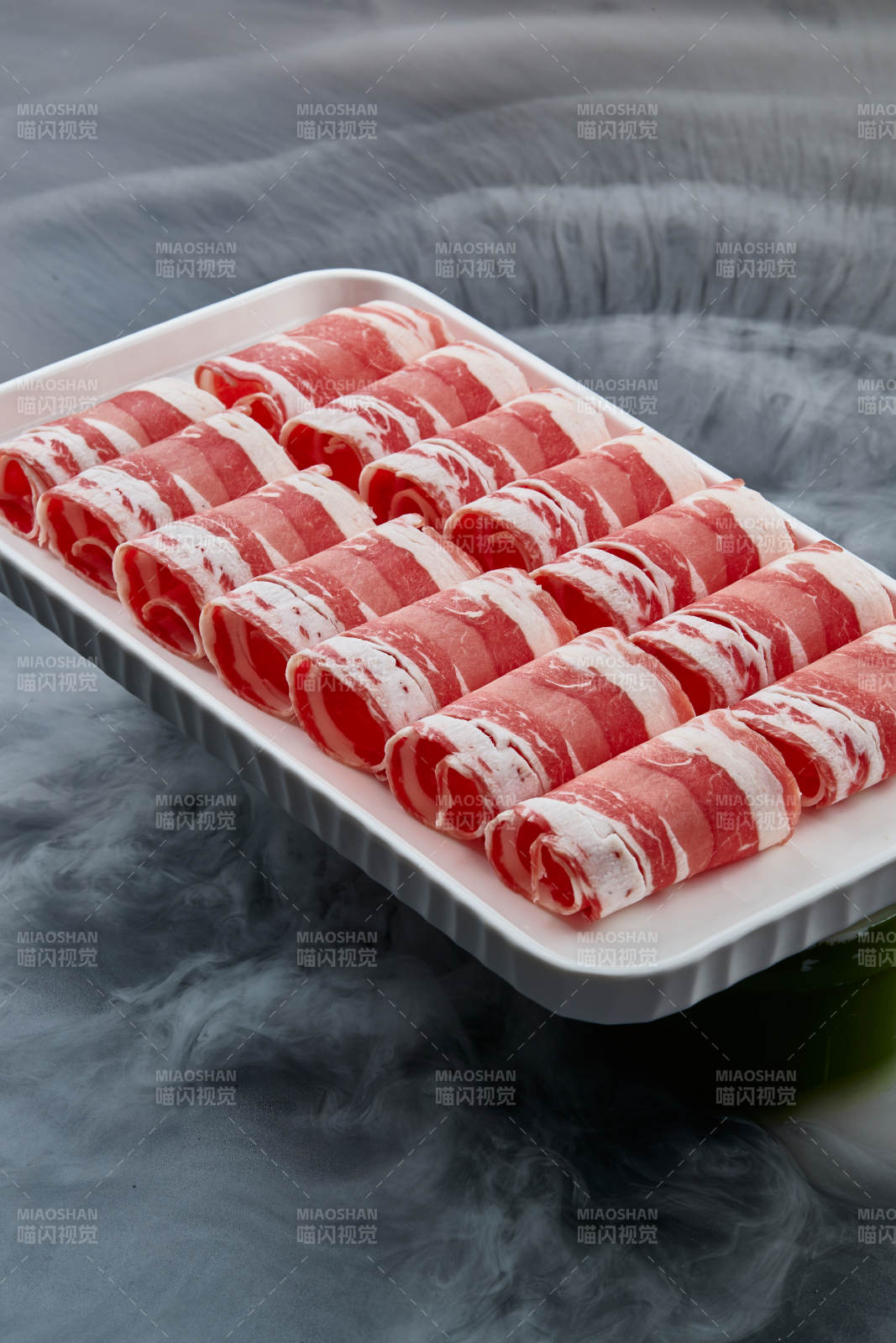 干冰缭绕的背景上摆放的草原肥羊肉卷图片
