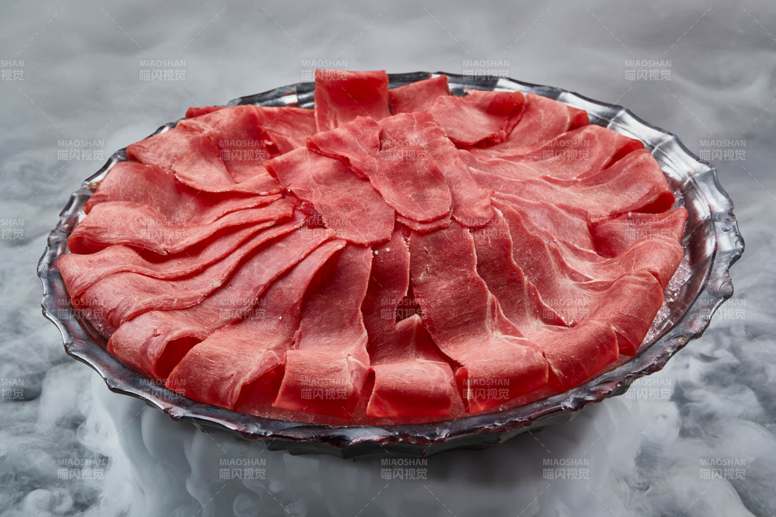 干冰缭绕的背景上摆放的鲜牛肉刺身图片