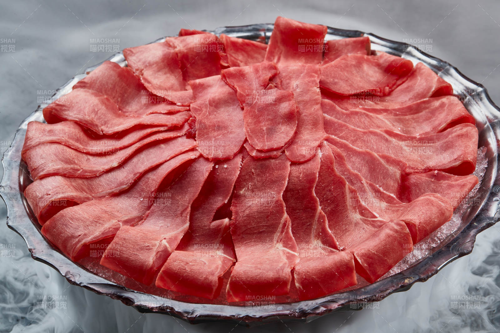 干冰缭绕的背景上摆放的鲜牛肉刺身图片