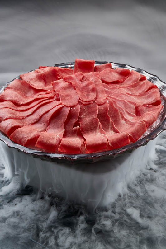 干冰缭绕的背景上摆放的鲜牛肉刺身图片