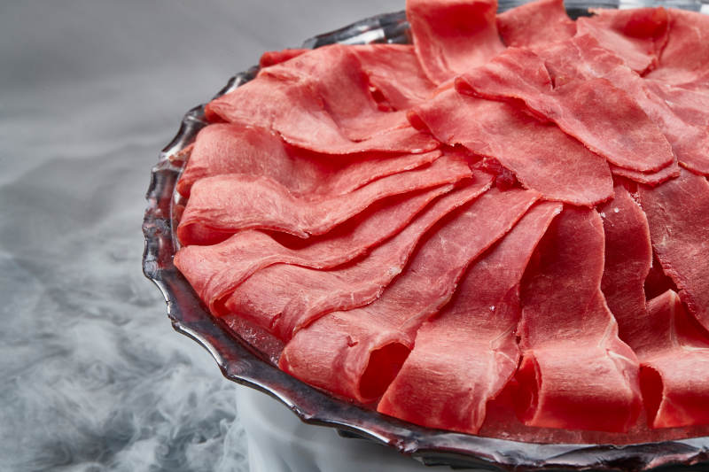 干冰缭绕的背景上摆放的鲜牛肉刺身图片