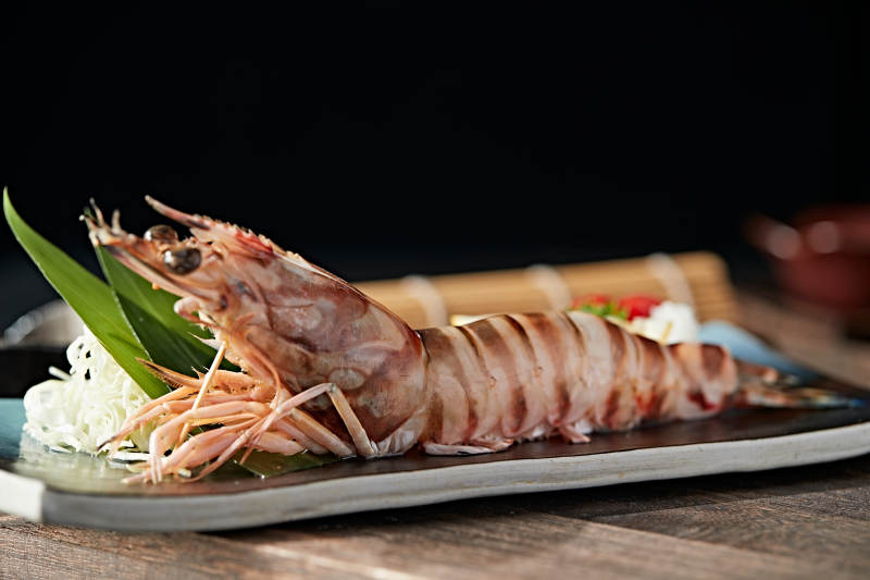 长方形瓷盘装的铁板野生明虾皇摆放在草垫上图片