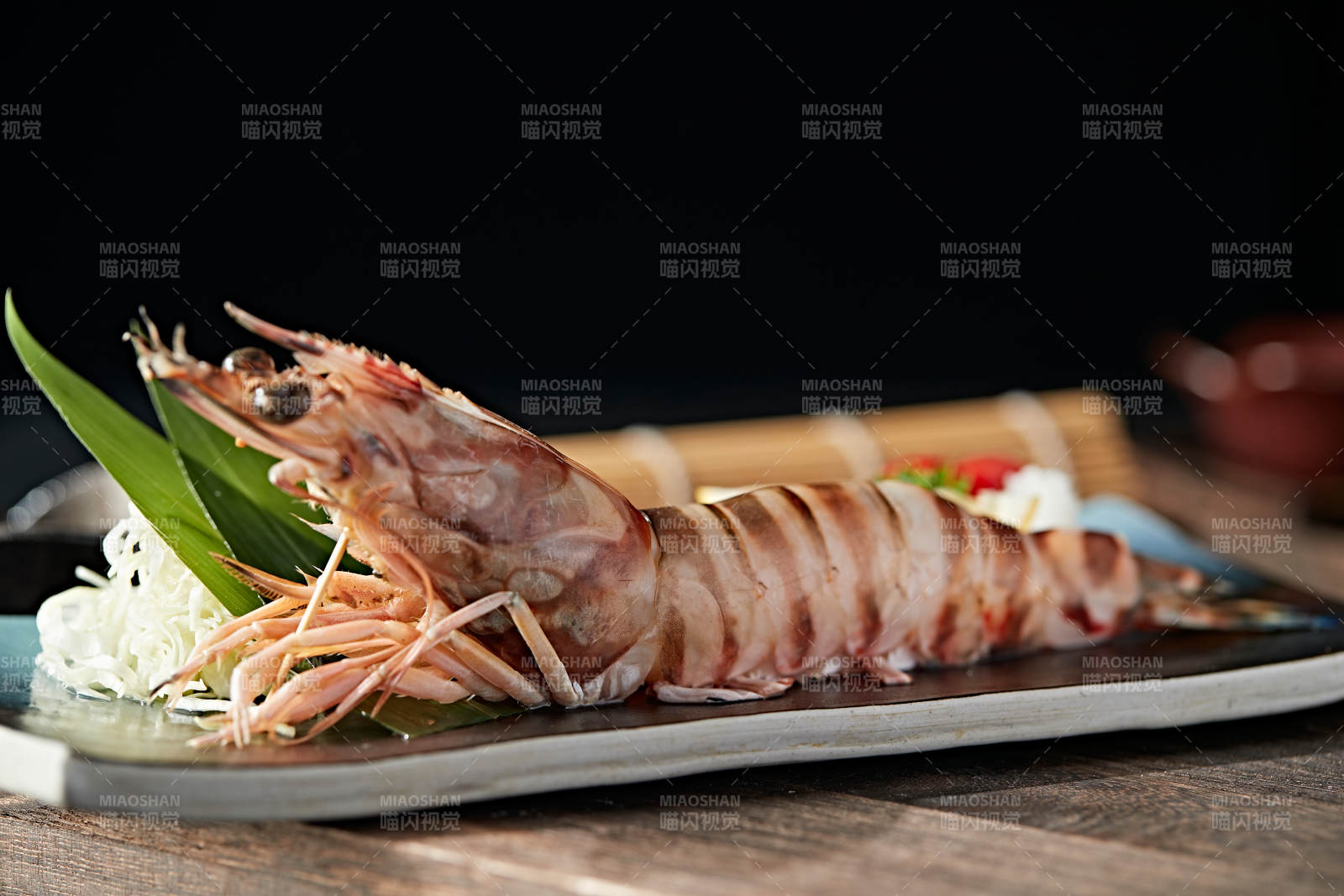 长方形瓷盘装的铁板野生明虾皇摆放在草垫上图片