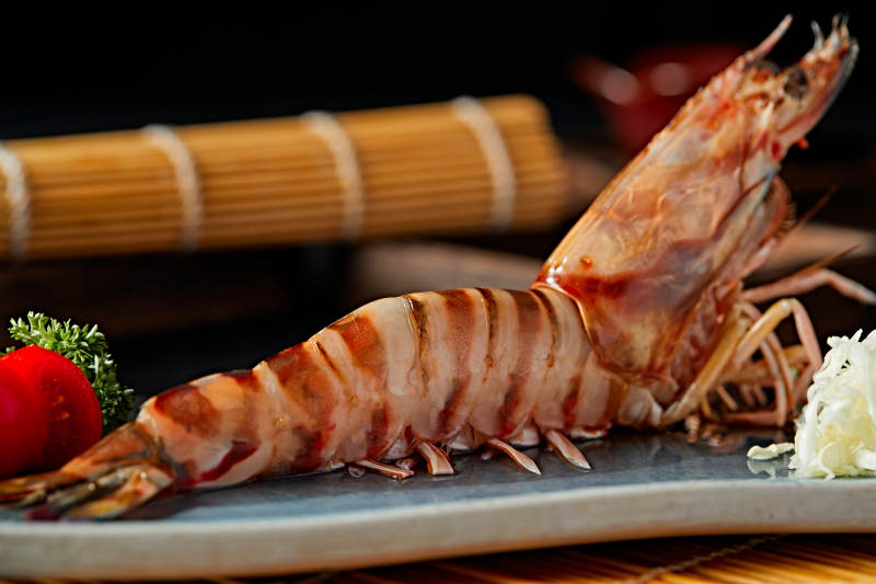 长方形瓷盘装的铁板野生明虾皇摆放在草垫上图片