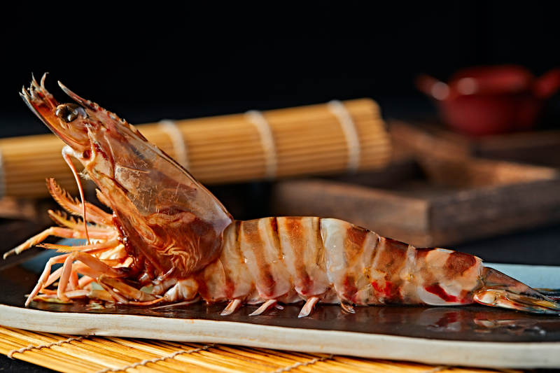 长方形瓷盘装的铁板野生明虾皇摆放在草垫上图片