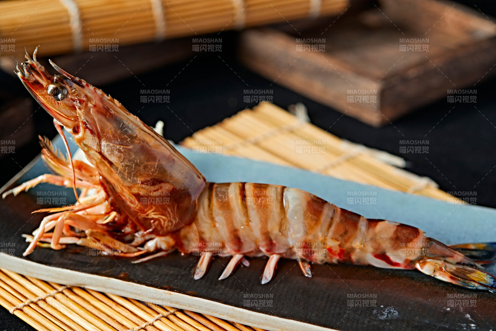 长方形瓷盘装的铁板野生明虾皇摆放在草垫上图片
