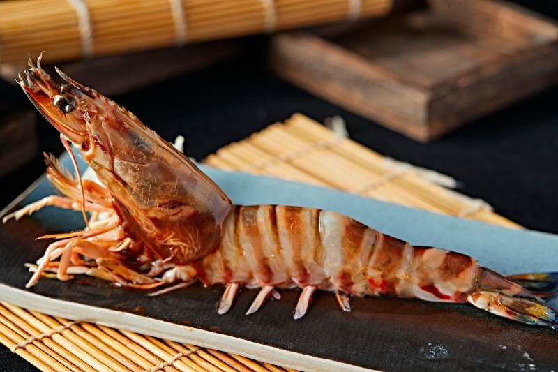 长方形瓷盘装的铁板野生明虾皇摆放在草垫上图片