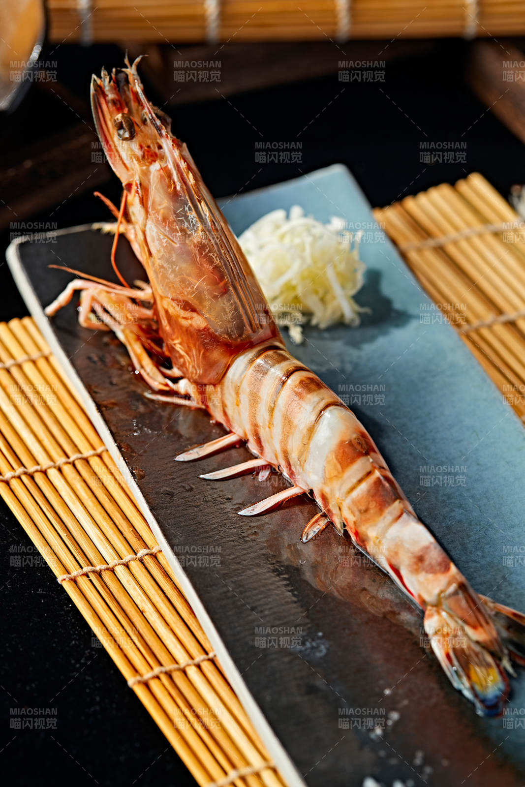 长方形瓷盘装的铁板野生明虾皇摆放在草垫上图片