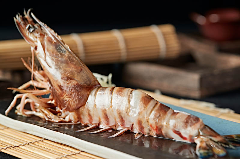 长方形瓷盘装的铁板野生明虾皇摆放在草垫上图片