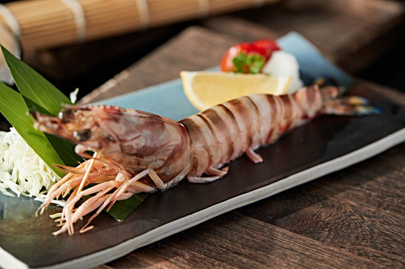 长方形瓷盘装的铁板野生明虾皇摆放在草垫上图片