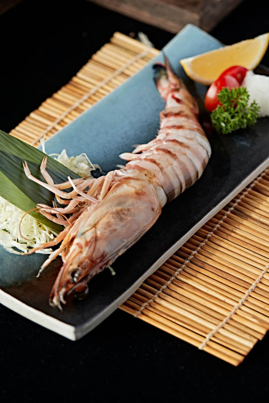 长方形瓷盘装的铁板野生明虾皇摆放在草垫上图片