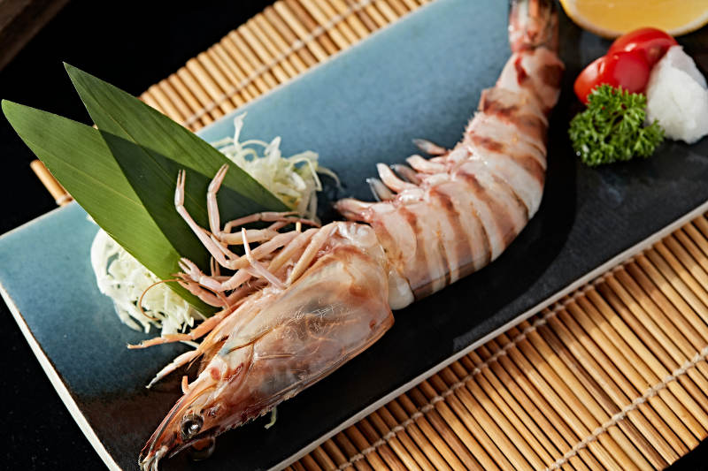 长方形瓷盘装的铁板野生明虾皇摆放在草垫上图片