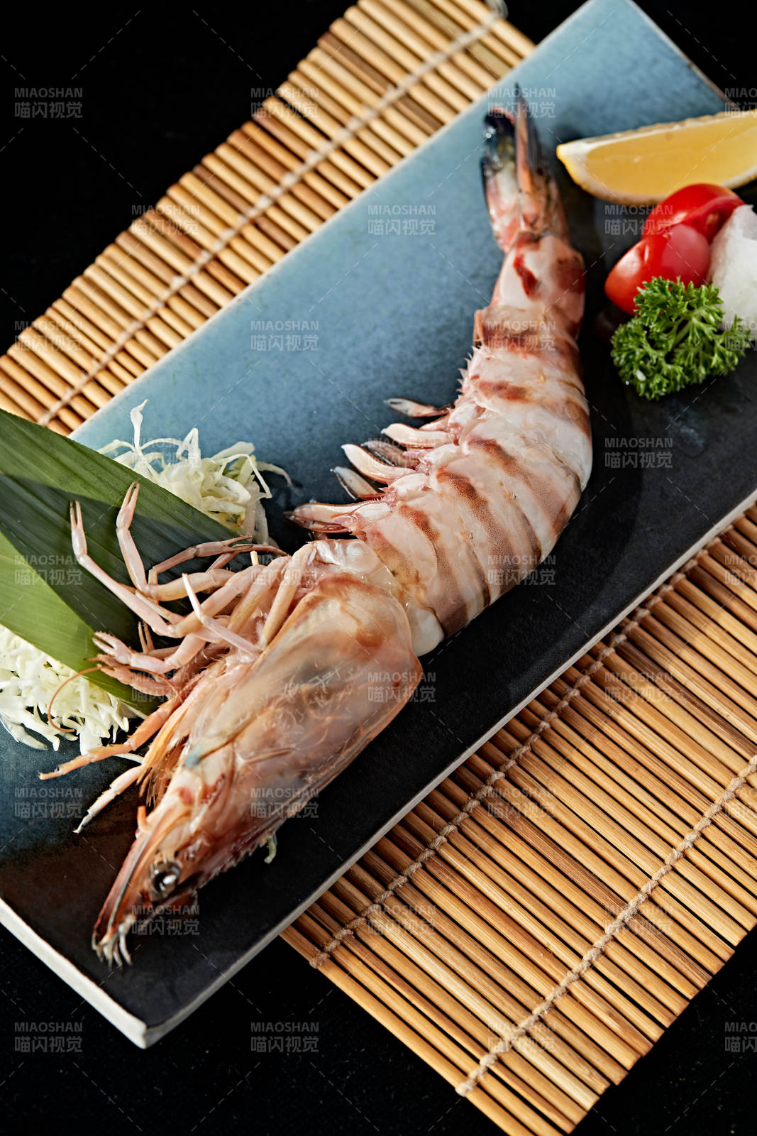 长方形瓷盘装的铁板野生明虾皇摆放在草垫上图片