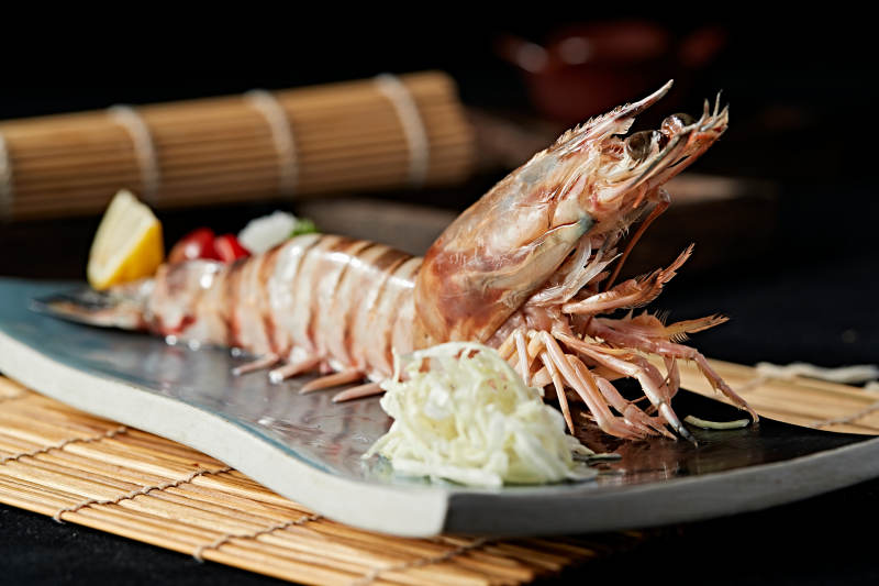 长方形瓷盘装的铁板野生明虾皇摆放在草垫上图片