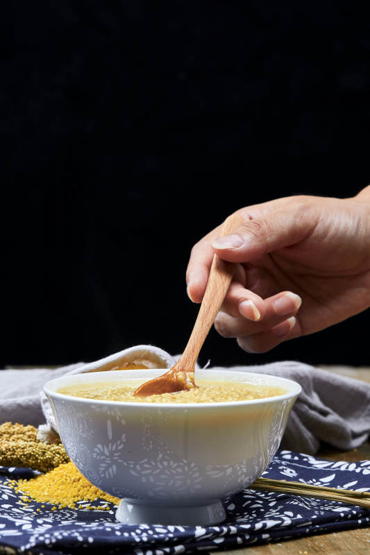 手持木勺㧟起的美味香浓小米粥图片