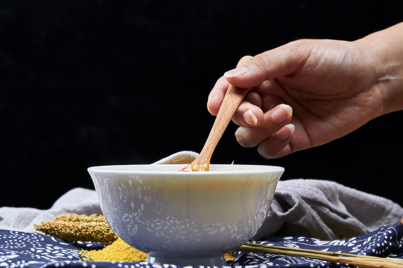 手持木勺㧟起的美味香浓小米粥图片