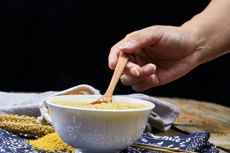 手持木勺㧟起的美味香浓小米粥图片