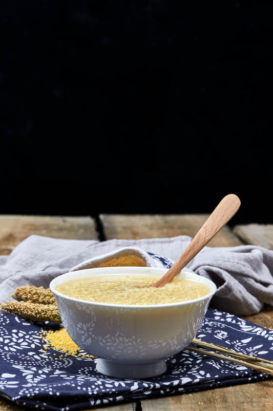 手持木勺㧟起的美味香浓小米粥图片