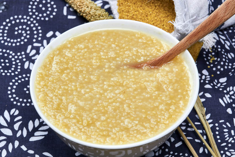 手持木勺㧟起的美味香浓小米粥图片