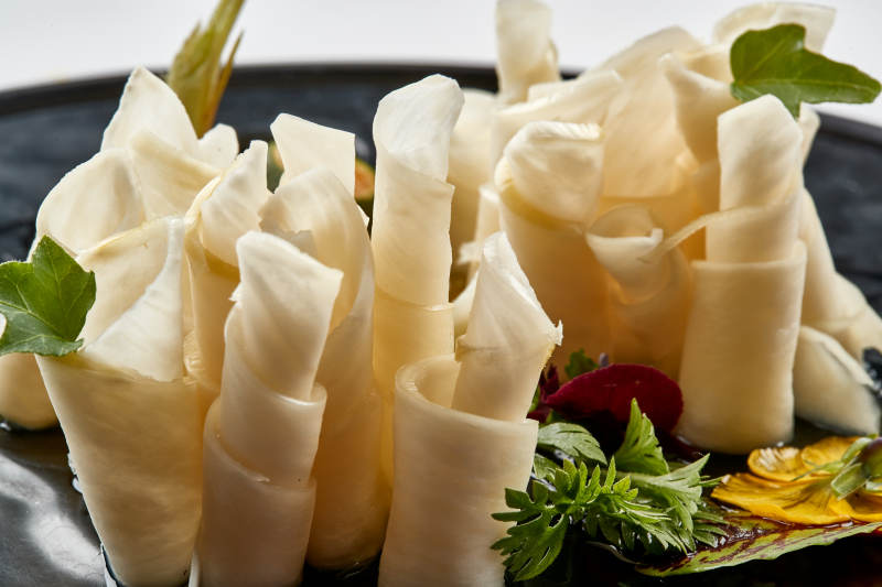 黑色瓷餐具装的鲜杏鲍菇刺身卷图片