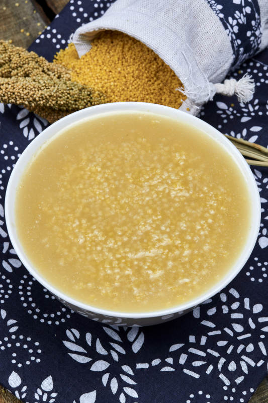 手持木勺㧟起的美味香浓小米粥图片