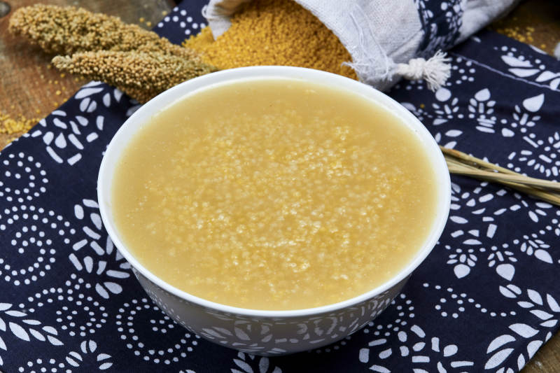 手持木勺㧟起的美味香浓小米粥图片