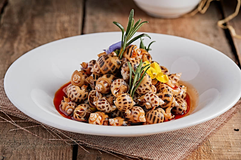 白色瓷盘装的红油腌渍小花螺图片