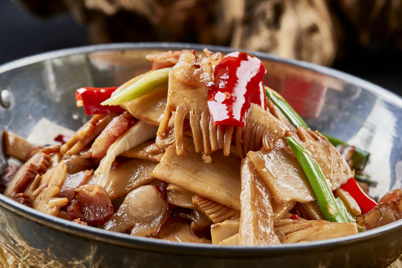 黑色背景上的锅仔香辣腊肉煲鲜笋图片