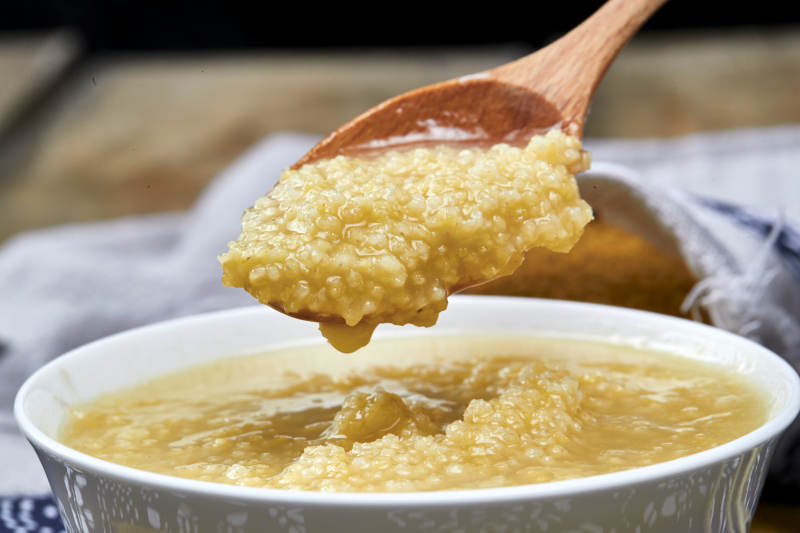 手持木勺㧟起的美味香浓小米粥图片