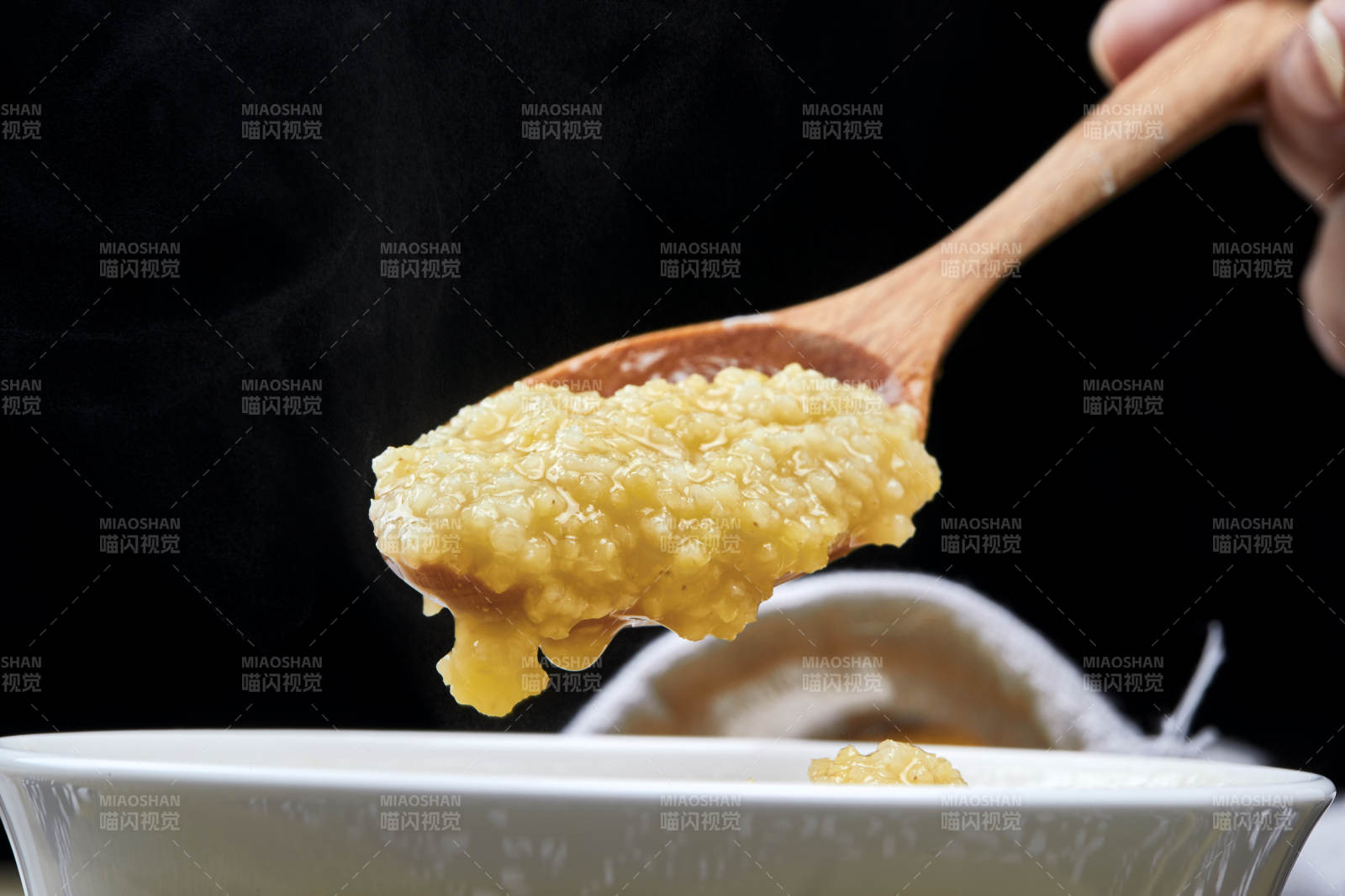 手持木勺㧟起的美味香浓小米粥图片