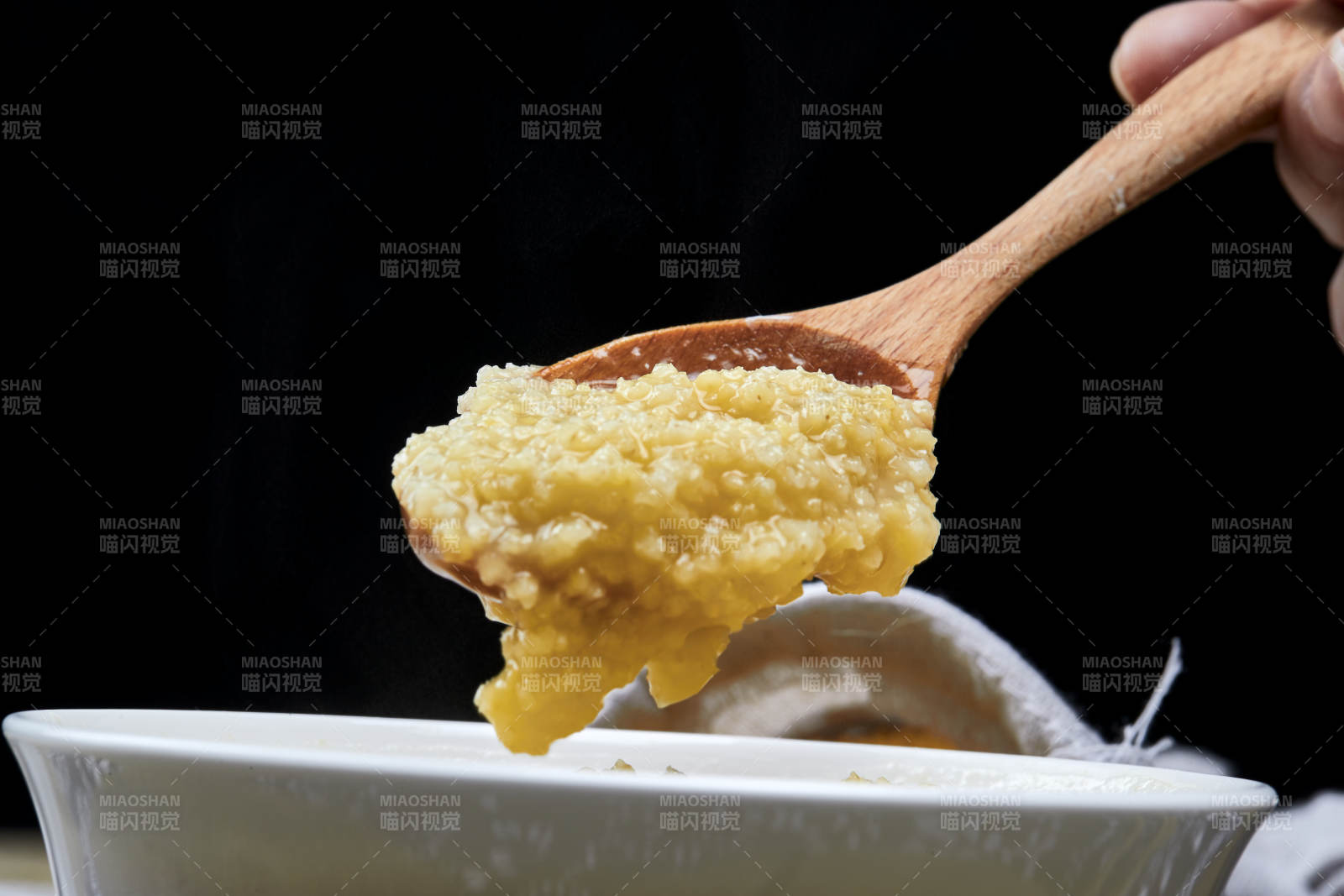 手持木勺㧟起的美味香浓小米粥图片