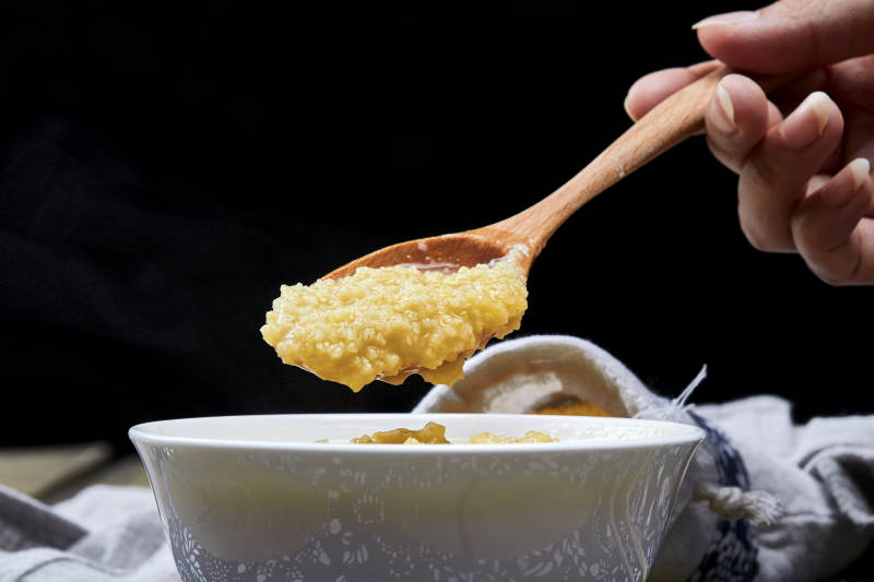 手持木勺㧟起的美味香浓小米粥图片