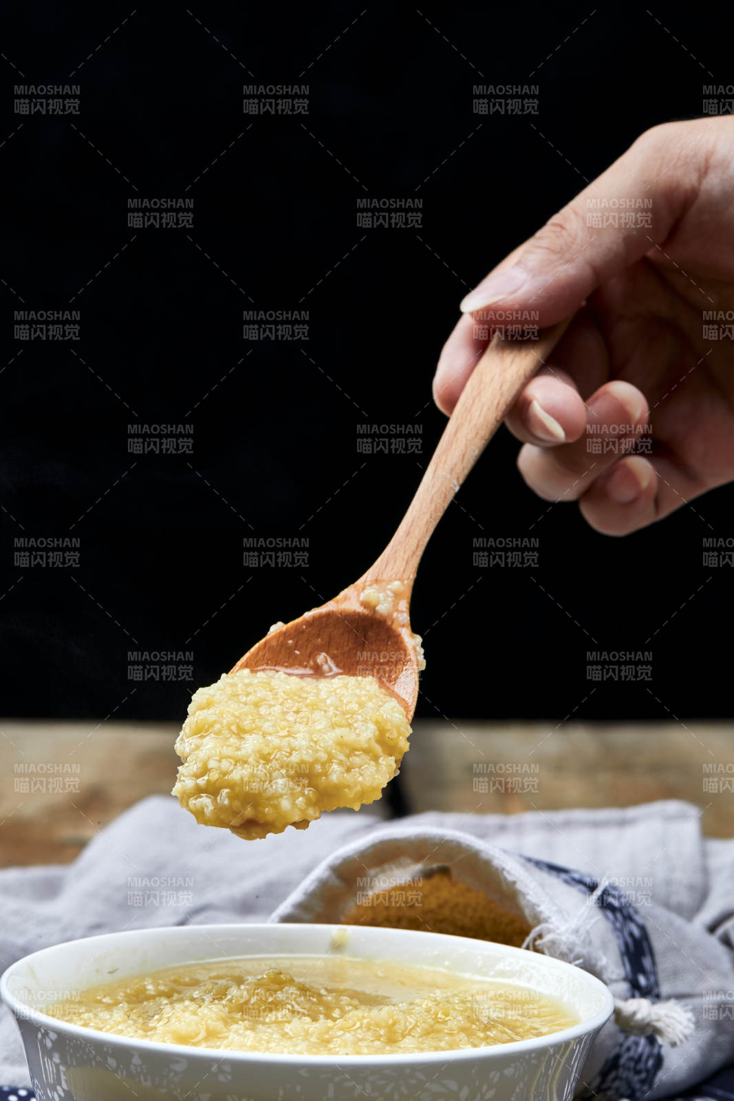 手持木勺㧟起的美味香浓小米粥图片
