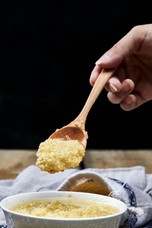 手持木勺㧟起的美味香浓小米粥图片