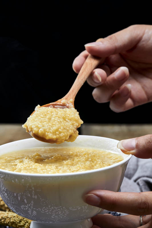 手持木勺㧟起的美味香浓小米粥图片