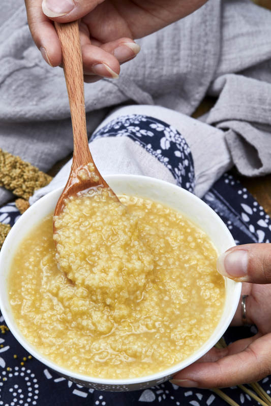 手持木勺㧟起的美味香浓小米粥图片