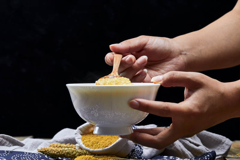 手持木勺㧟起的美味香浓小米粥图片