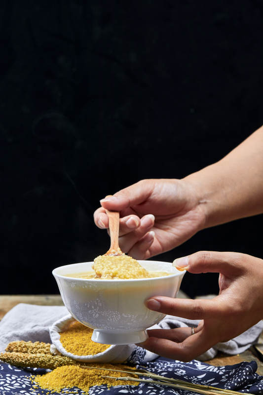 手持木勺㧟起的美味香浓小米粥图片