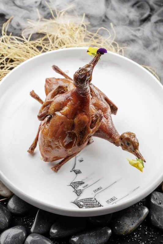 白色圆盘装的生炸乳鸽摆放在黑色鹅卵石上图片