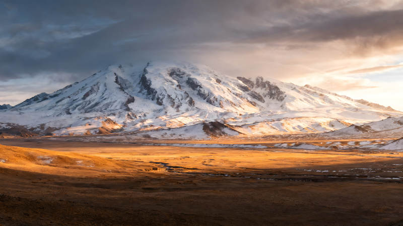 雪山下的金色平原阳光照射下的壮丽景色图片