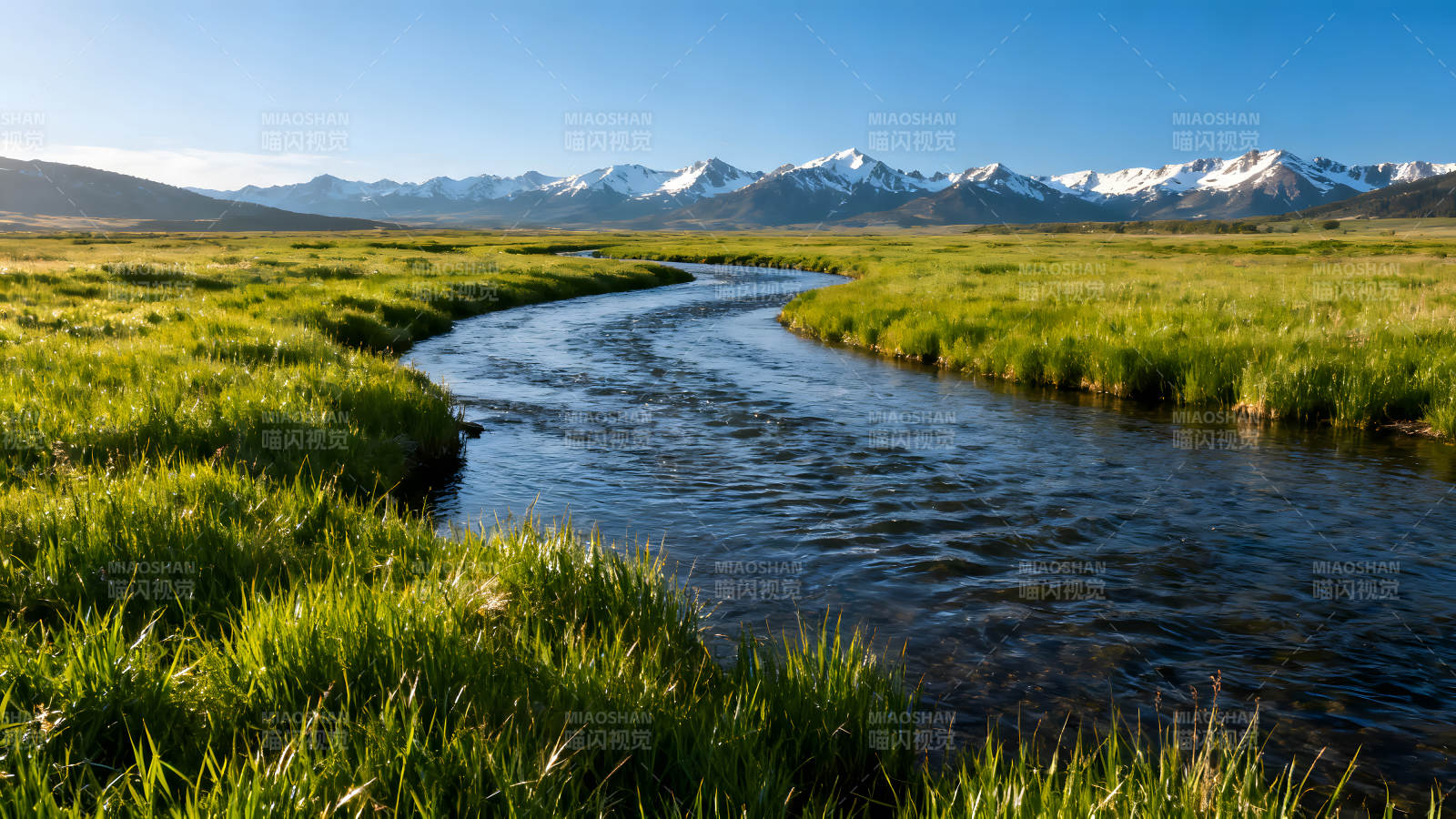 蜿蜒河流穿过青翠草地雪山映衬图片