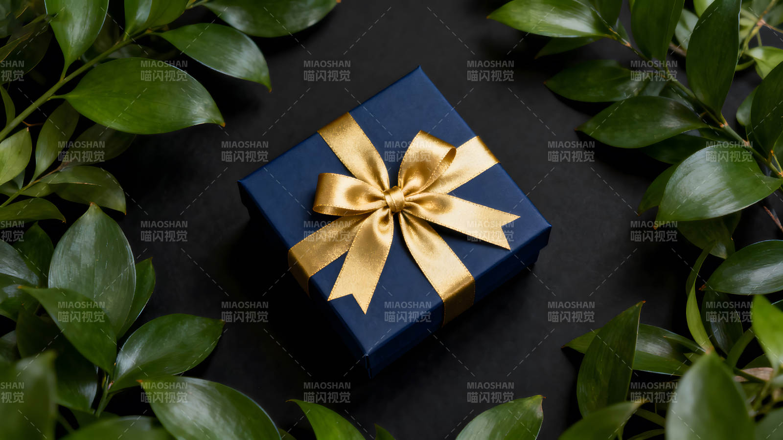 蓝色礼盒配金色蝴蝶结与绿叶图片