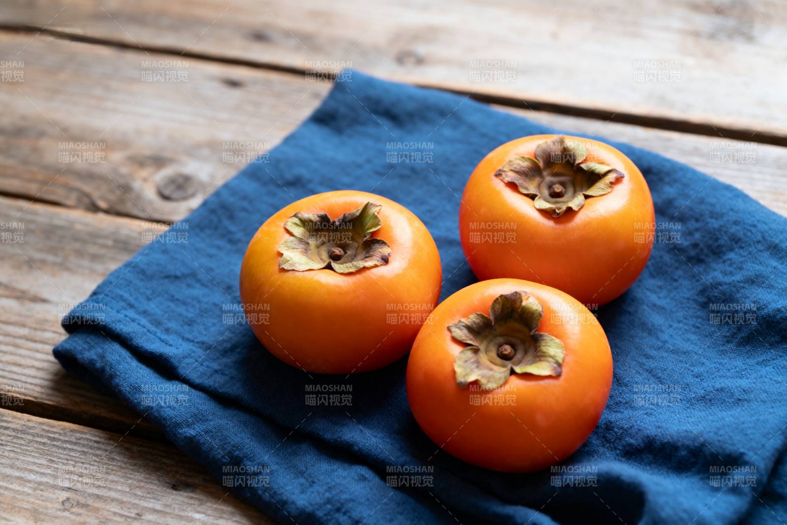 三颗柿子静置蓝布上图片