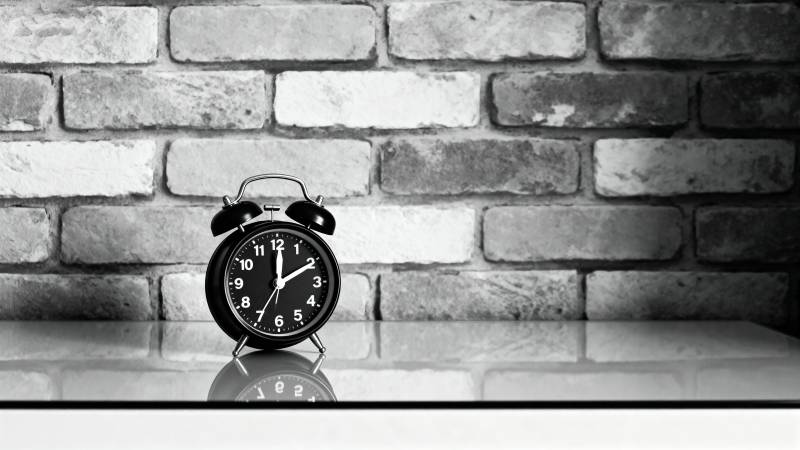 复古闹钟静置砖墙前图片