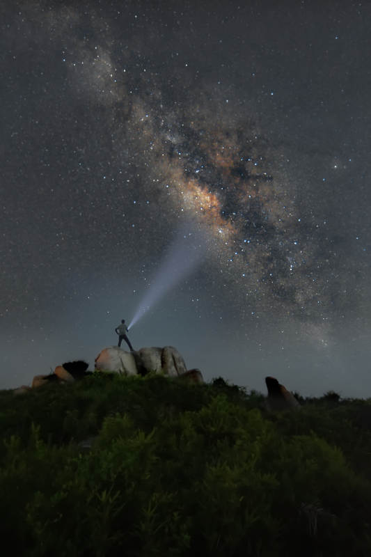星空银河下的一个人举着探照灯图片