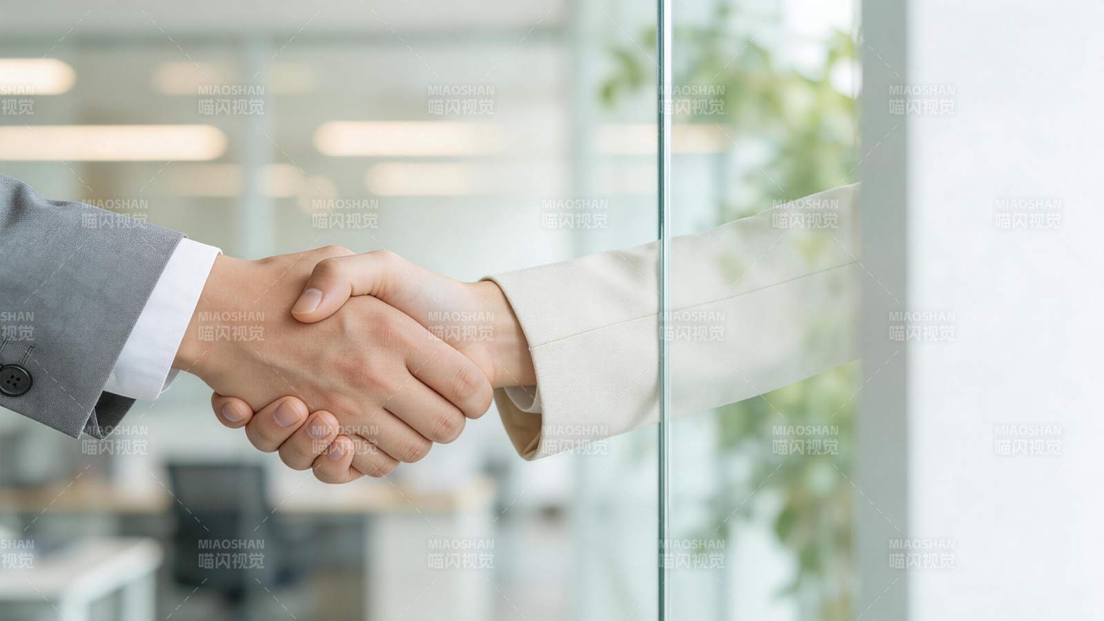 办公室玻璃隔断前两人握手合作场景图片