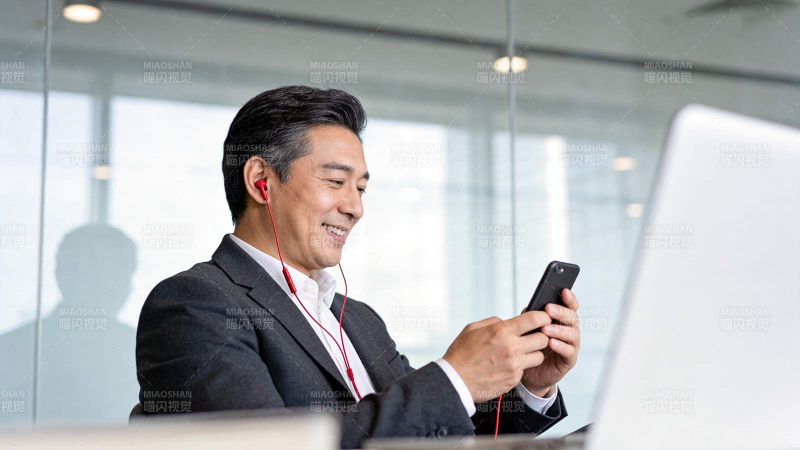 穿西装男子戴红耳机看手机微笑工作图片