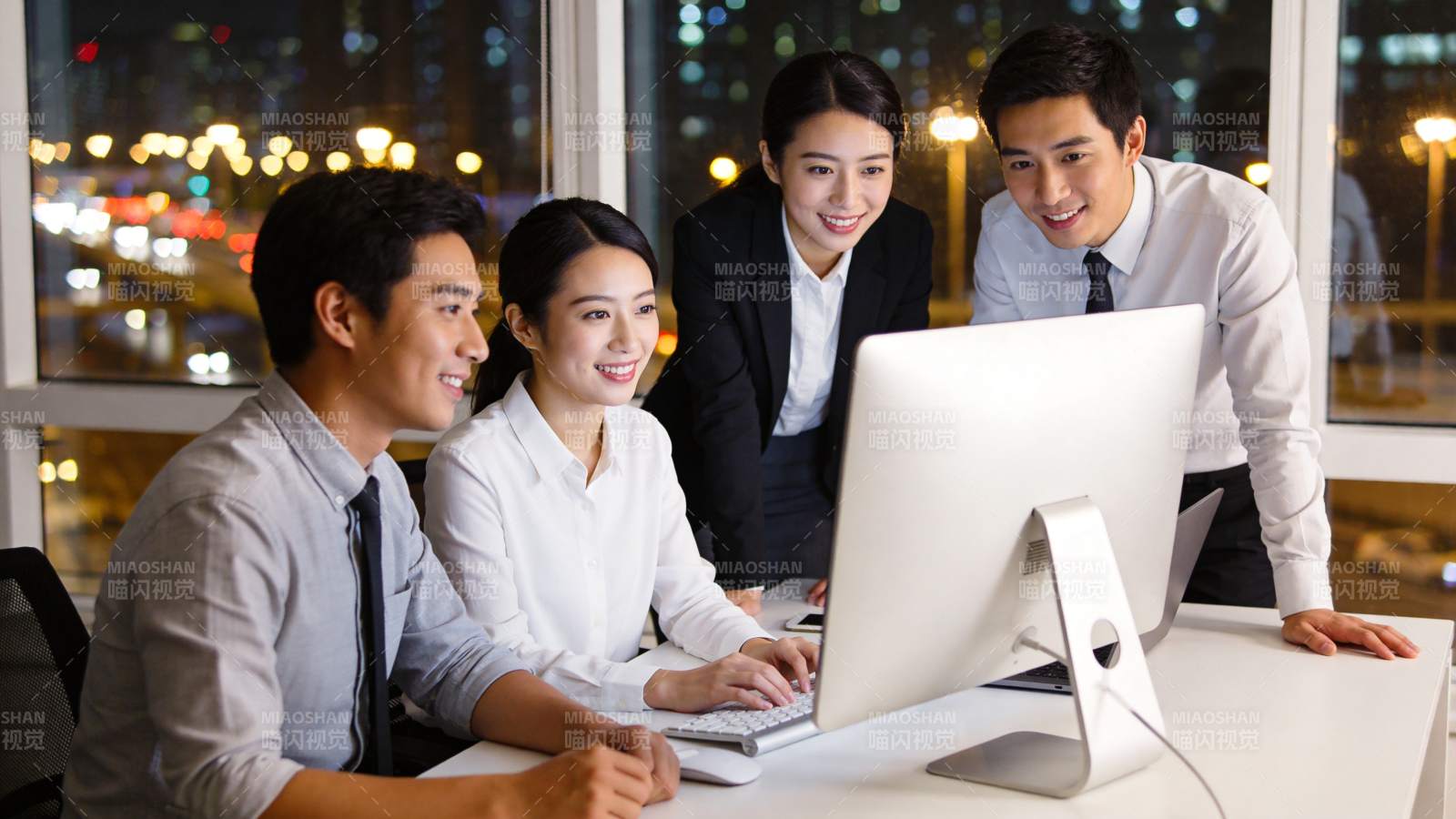 四位职场人员围坐电脑前协同工作场景图片