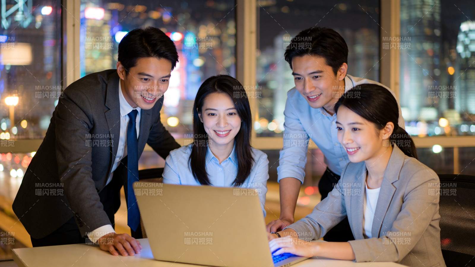 四位职场人士围看笔记本电脑讨论工作图片