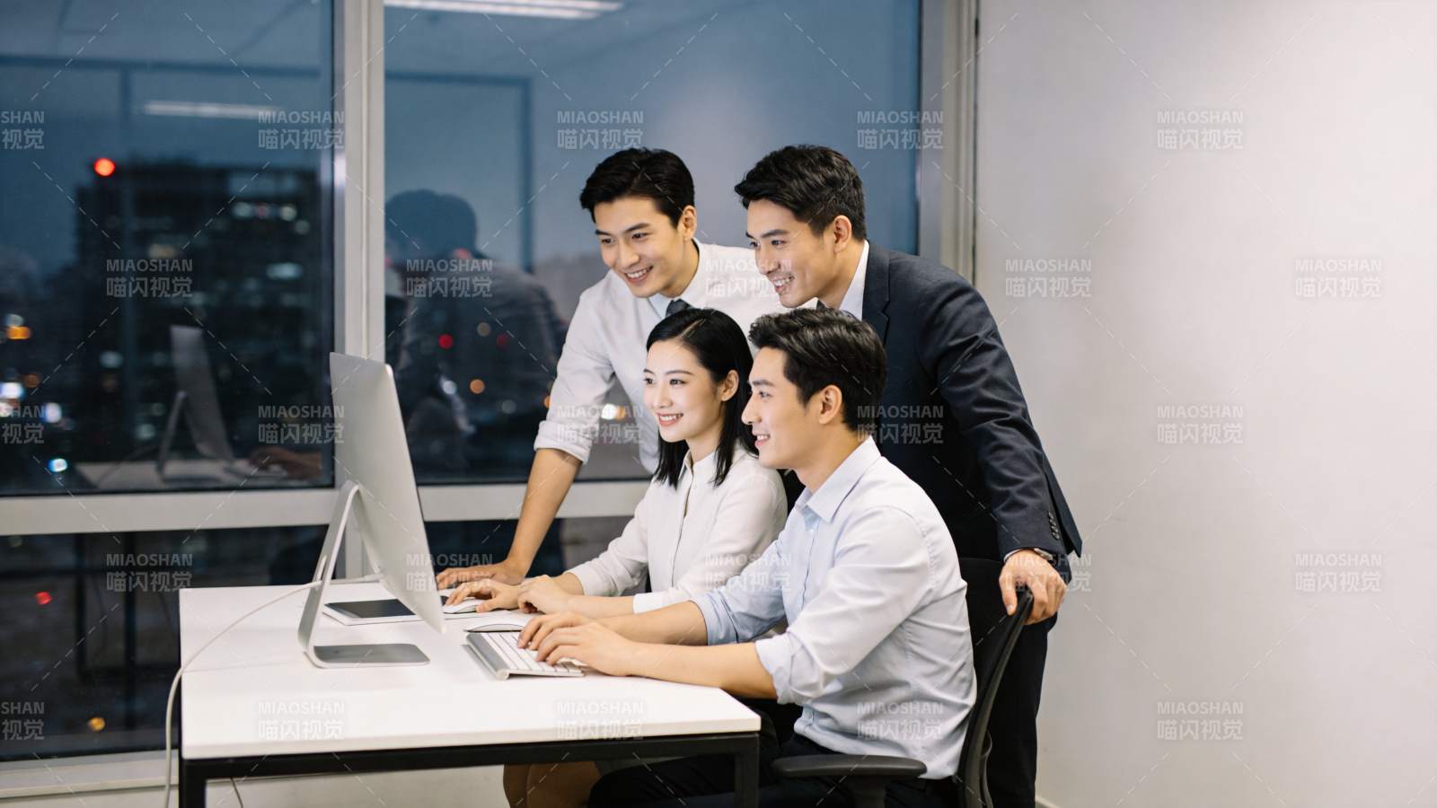 四名职场人员围坐电脑前协同工作场景图片